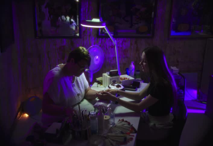 A middleaged woman applies nail polish to a young womans fingernails inside a beauty shop