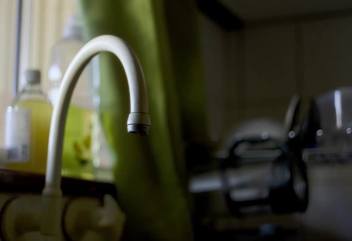 Water drips from a kitchen sink faucet near a window