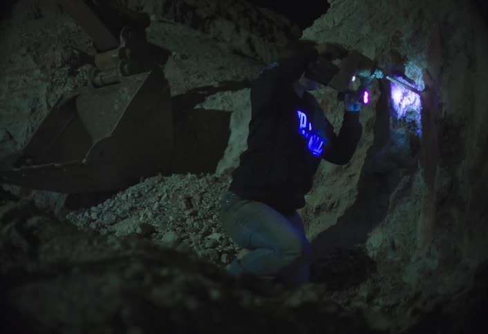 Cave explorer holds a flashlight and uses a drill to make a hole inside a cave