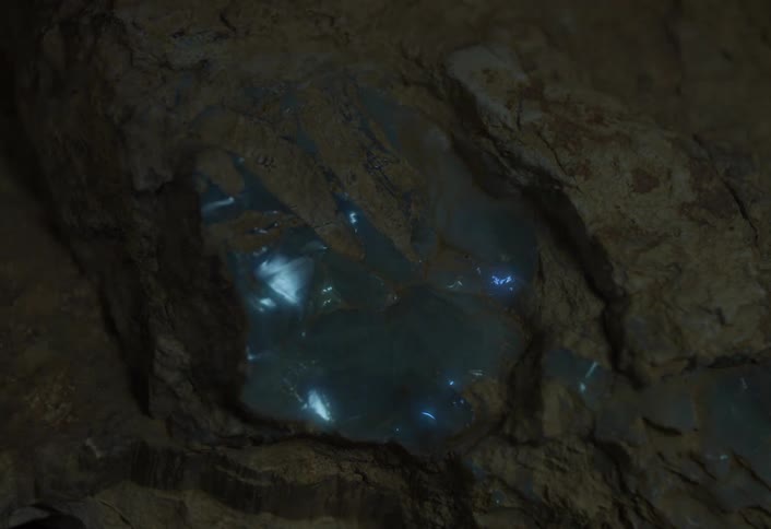 A closeup of a glowing blue crystal embedded in rough brown rock