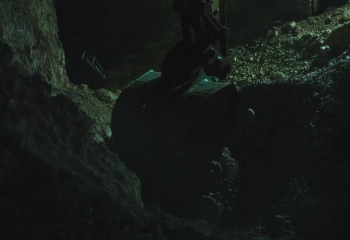 A backhoe digs into dirt filled with rocks at night