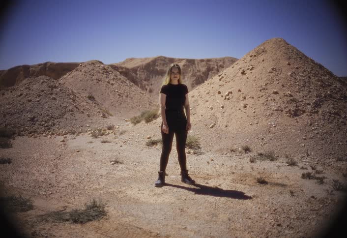 A woman stands alone in a rocky desert landscape under a clear blue sky