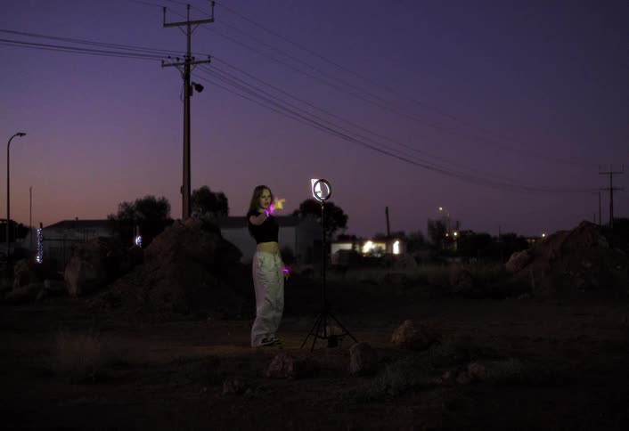 Woman dances at night in an open area lit by a ring light