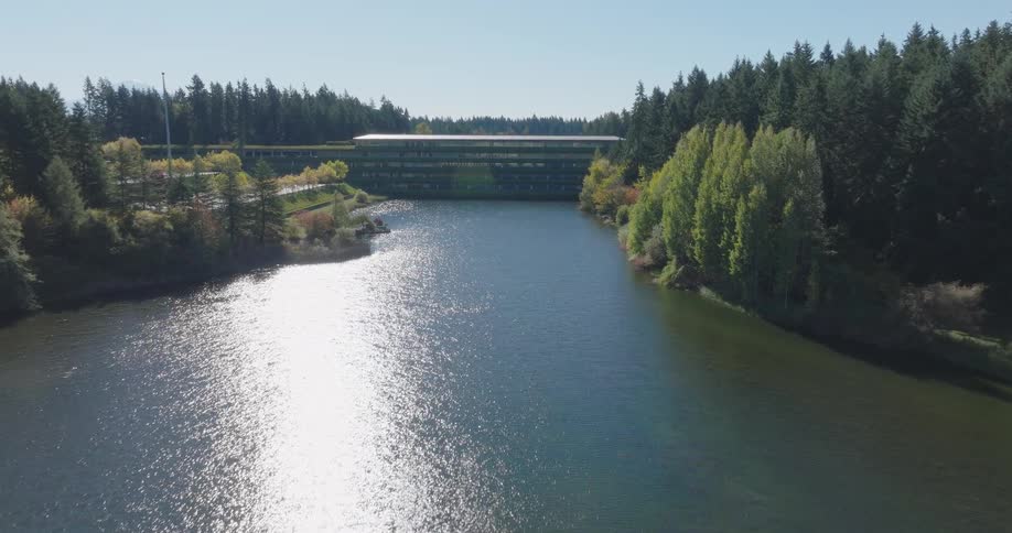 Flying through a beautiful office park over a shimmering lake surrounded by peaceful green space and large trees