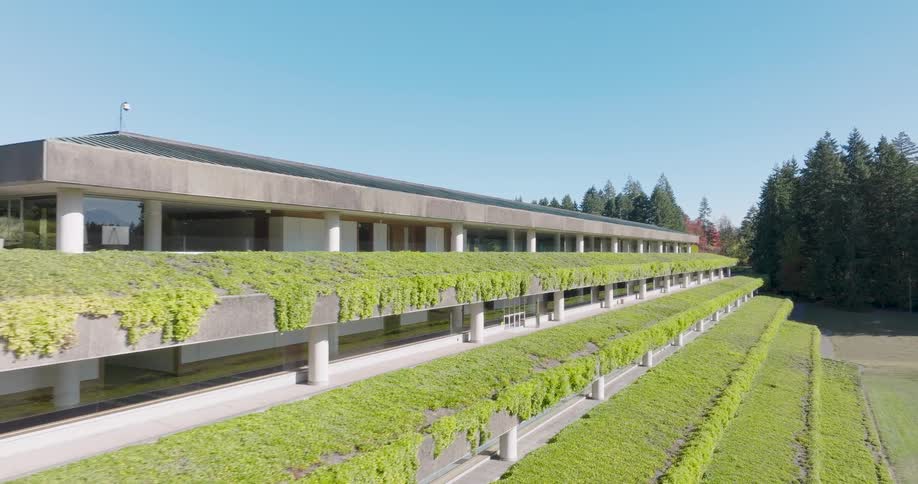 Parallel traverse along the facade of a modern green office building surrounded by trees and blue skies