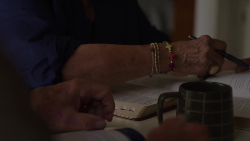Close up of an elderly woman reading a bible while sitting at a table indoors during daytime