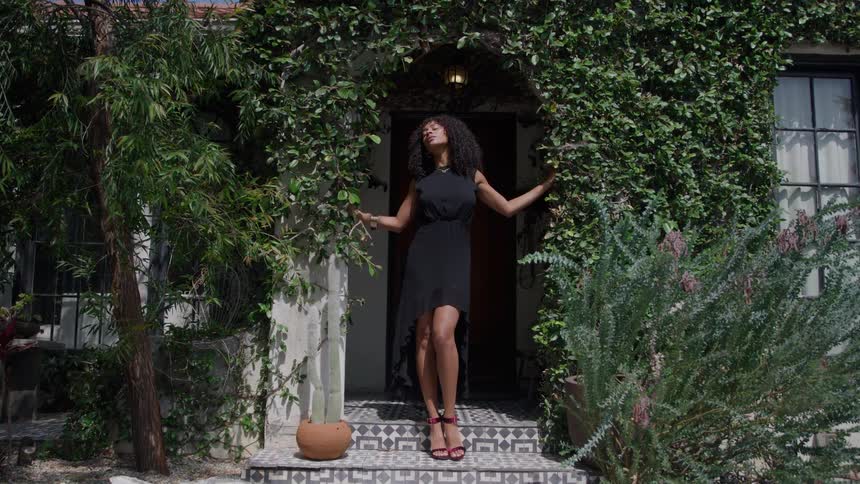A woman poses in a doorway surrounded by lush green vines on a sunny day