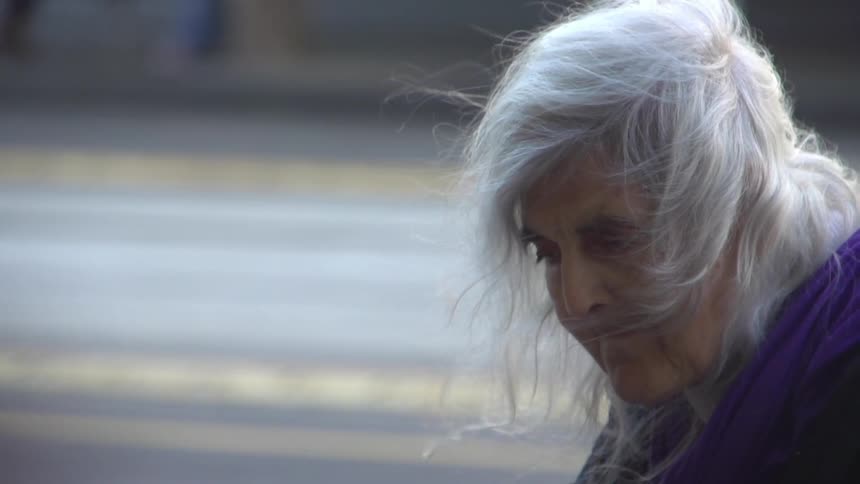 An elderly woman next to a street as the wind blows her hair in her face