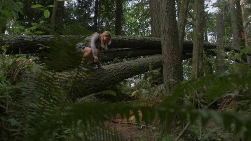 A woman is climbing over trees in the forest