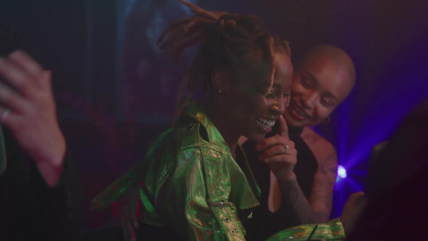 Two women at a party one taking a selfie with her phone while the other kisses her on the cheek