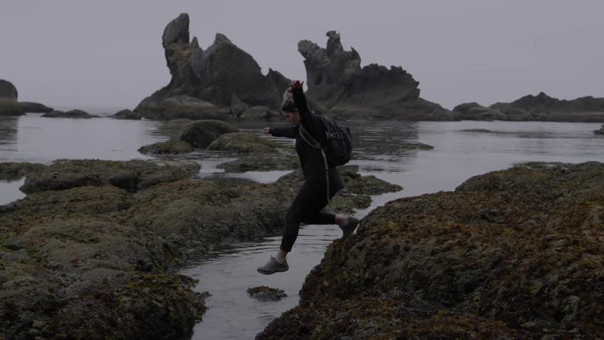 Woman hopping across rocks at the ocean