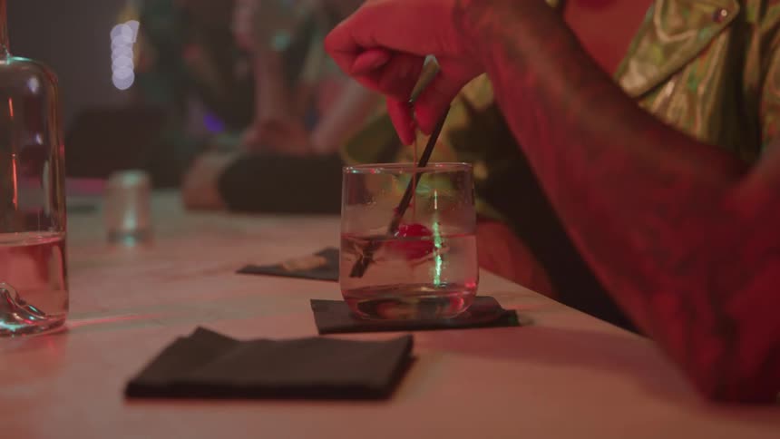 A group of friends having drinks at a bar while a man with a tattooed arm spins the drink in his glass