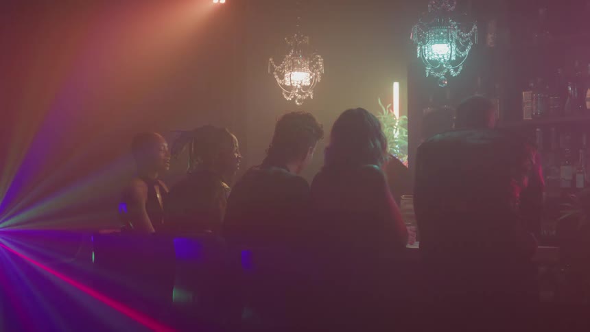 People sitting at a bar lit by colorful lights and hanging chandeliers