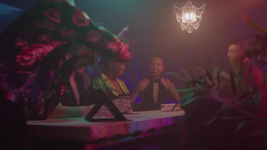 Group of friends chat and laugh in a bar with colorful lighting and a relaxed atmosphere