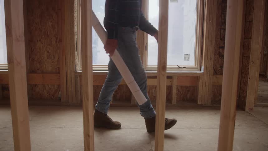 The man walks through the home frame with blueprints