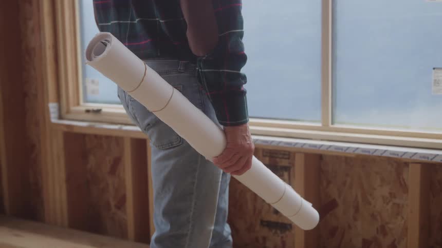The man is holding blueprints in the home