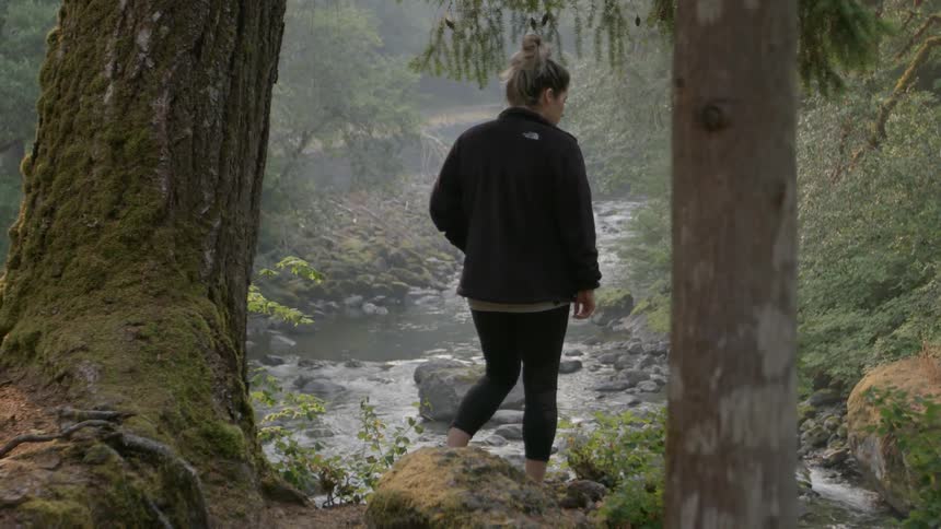 A woman walks by a stream in the wilderness