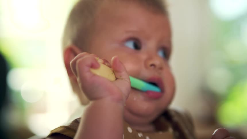 Curious baby holds a colorful spoon in their mouth