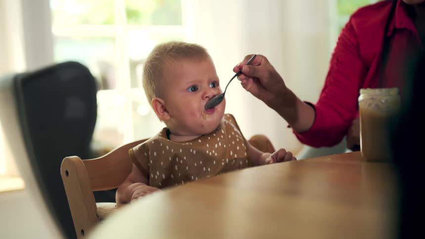 A mother feeding her baby while sitting at the dining table at midday