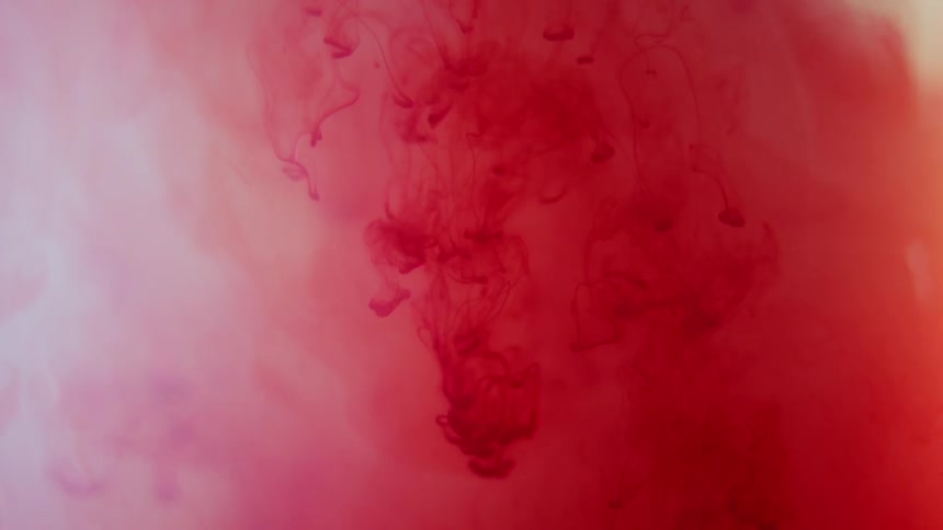 Red and crimson ink slowly flows and spreads downward through pale pink liquid creating dark wispy vertical patterns and organic textures against a warm light orange edge