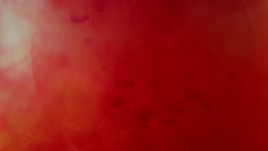 Close up liquid red ink slowly drips downward through a watery medium blending into rich crimson and orange colors creating a vibrant abstract background texture