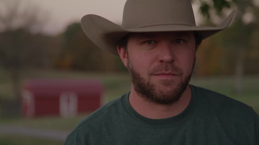 Man wearing a cowboy hat in a rural area at dusk