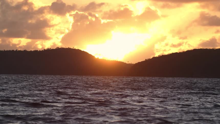 Water ripples and waves as the sun glows brightly over mountains along the coast