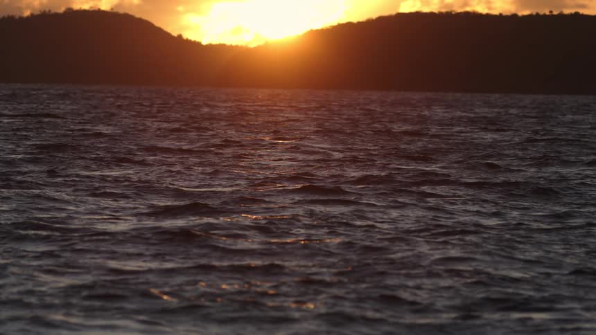 Sun sets behind the hills reflecting golden tones over the sea