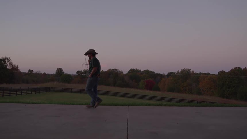 A man in a cowboy hat paces back and forth outdoors at a ranch