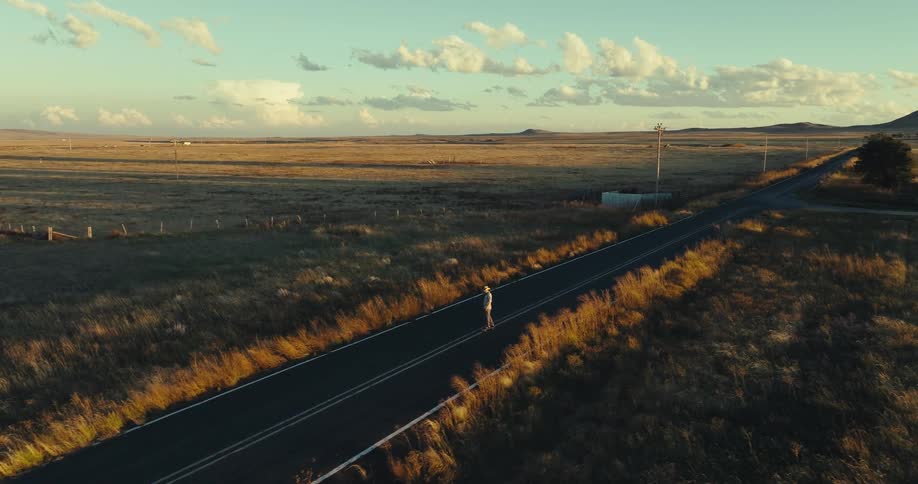 A person skateboards down an empty country road at sunset