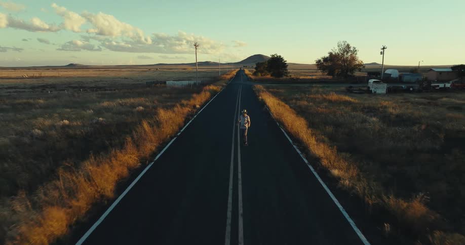 Person rides a skateboard alone on a deserted road at sunset