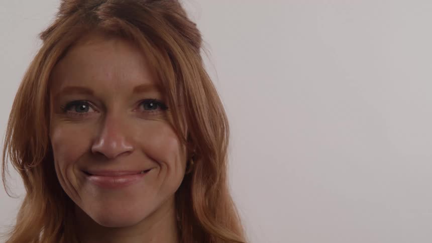 A young woman with red hair inside a room with whitepainted walls has a brief smile on her face