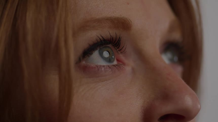 A very tight macro shot focuses on the eyes of a person with long dark eyelashes and a visible iris color in a indoor blurred setting