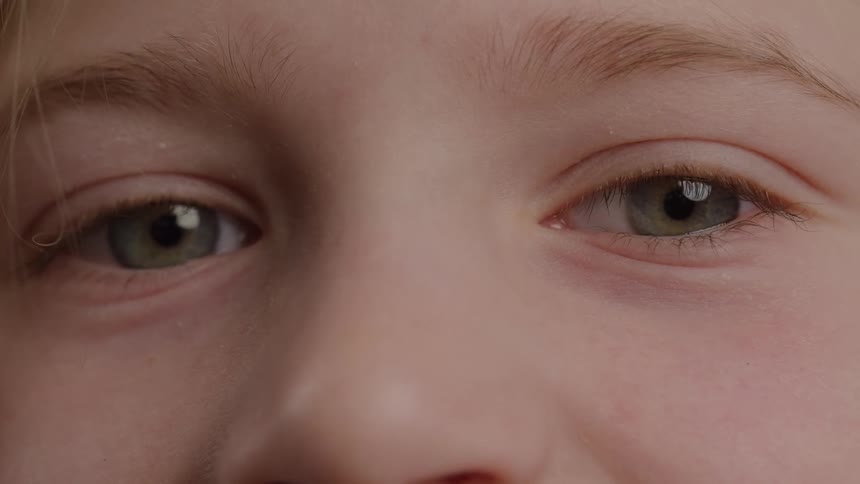 A child with green eyes looks calm in an extreme closeup of their face