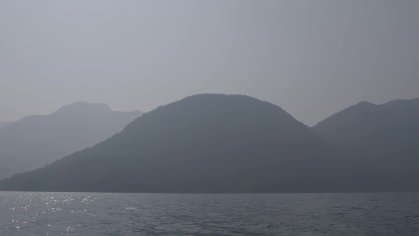 Moving view of a large body of water with some big hills in the background on a hazy day