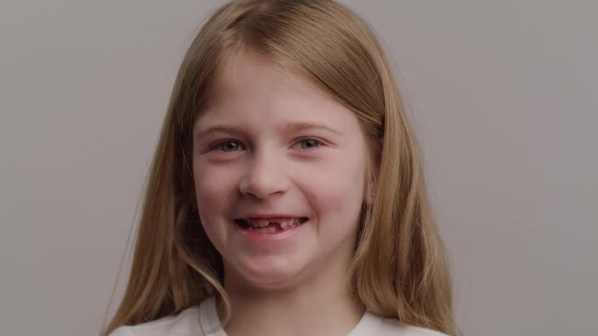 A closeup shot features a smiling young girl with long blonde hair and blue eyes looking directly at the camera she displays a gap where one of her front teeth is missing