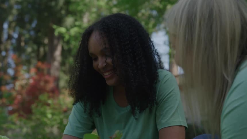 Two young women smile at each other while working together in the garden
