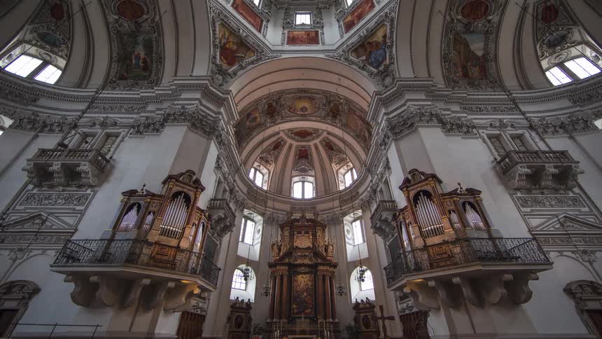 The video begins with a view of the ornate interior of a church showing rows of wooden chairs and a polished floor inscription the camera slowly tilts up to reveal the magnificent highly decorated domed ceiling and the detailed architectural features a
