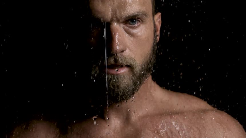 Water drips off the face of a man standing outdoors under the rain at night