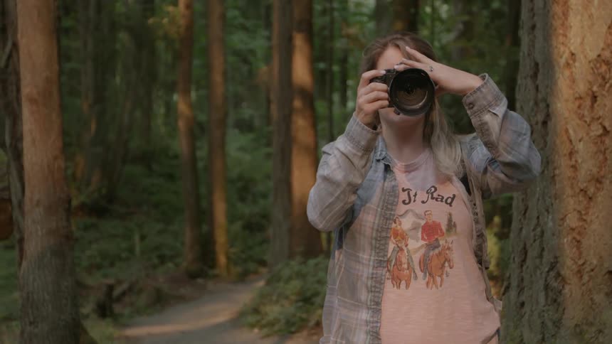 A woman holds a camera in a forest