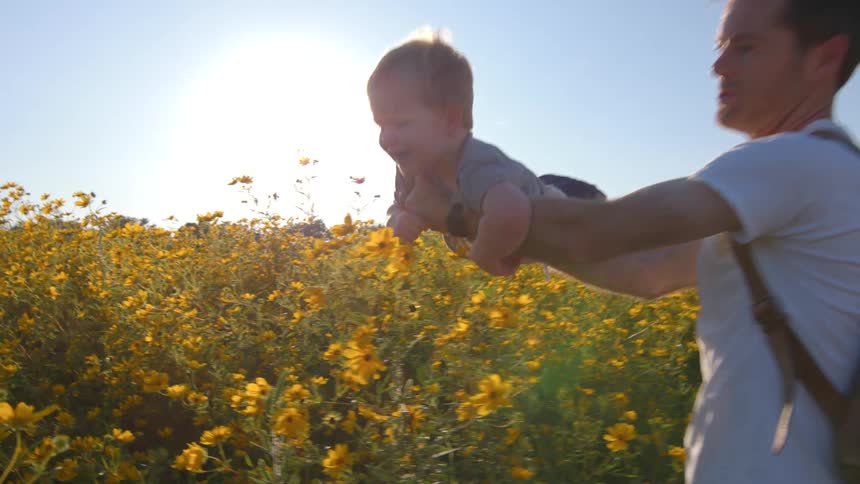 A man holding a baby in his lap is having fun carrying it in a sunflower field