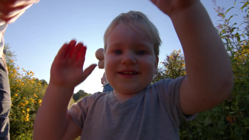 A child standing in a field with his father and mother smiles playfully as he opens and closes a box