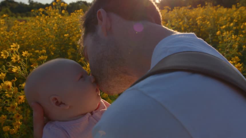 Father holding baby in a bright yellow flower field