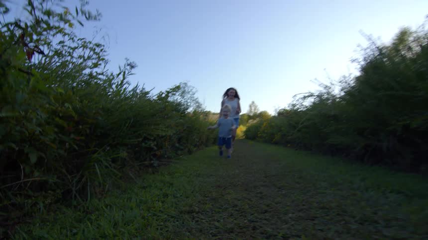 Mother and son run playfully along a grassy path surrounded by greenery