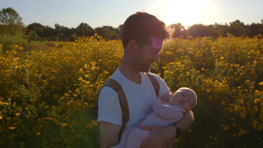 A father holds his baby daughter while standing in a field of yellow wildflowers