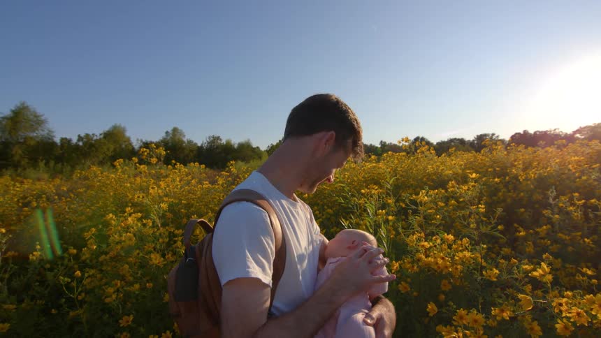 A father holds his baby daughter while standing in a field of yellow wildflowers