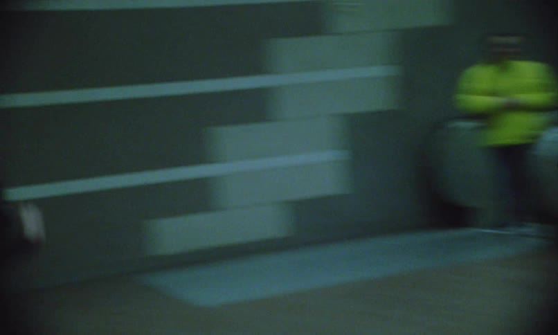 A young man and a young woman running in a subway station and going down an escalator