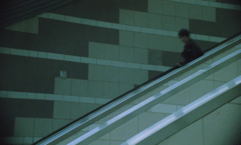 Two people wearing black clothes are running on an escalator