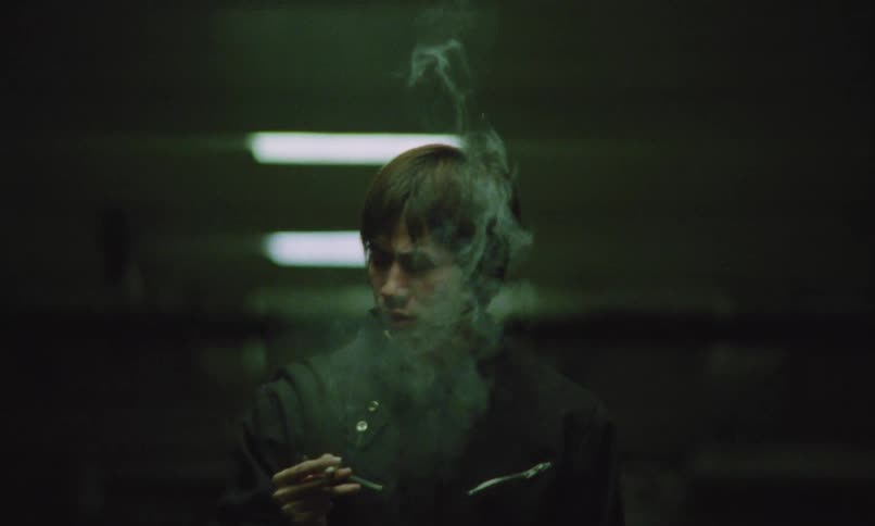 Asian man wearing black clothes smoking a cigarette indoors
