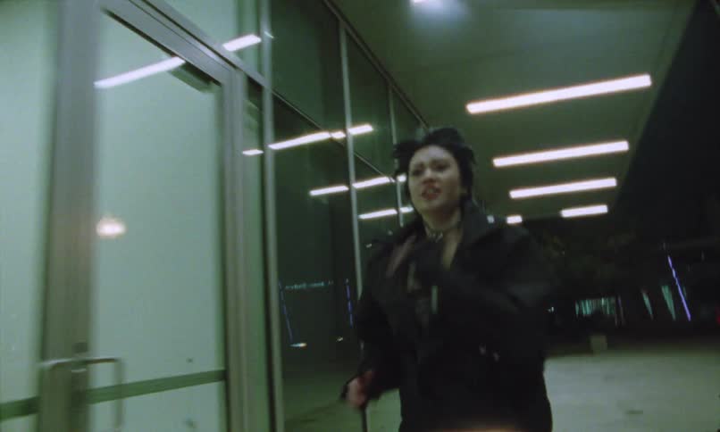 A person runs at night beneath bright ceiling lights beside glass doors